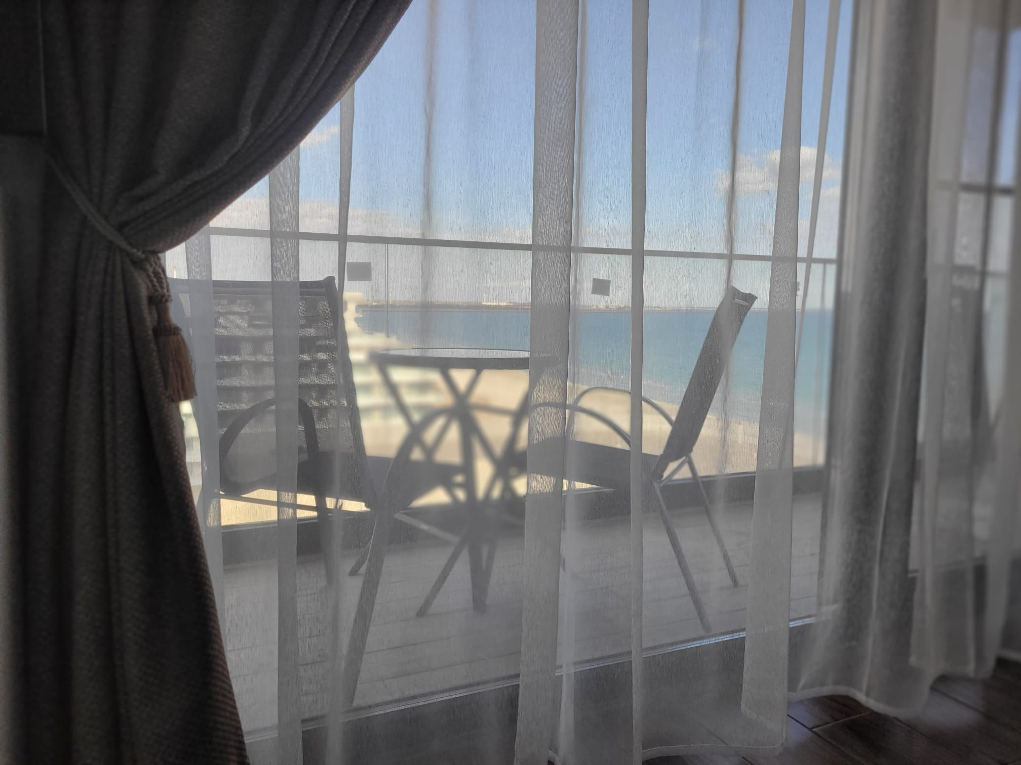 Balconul — prins prin perdele, cu lumină naturală și vedere la mare